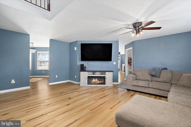 living area featuring a glass covered fireplace, baseboards, wood finished floors, and a ceiling fan