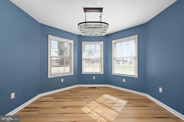 unfurnished room featuring baseboards, a notable chandelier, and wood finished floors