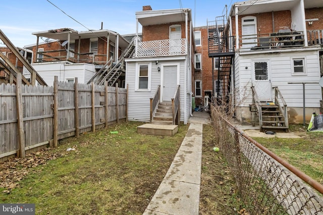 back of house with entry steps, a yard, brick siding, and a fenced backyard