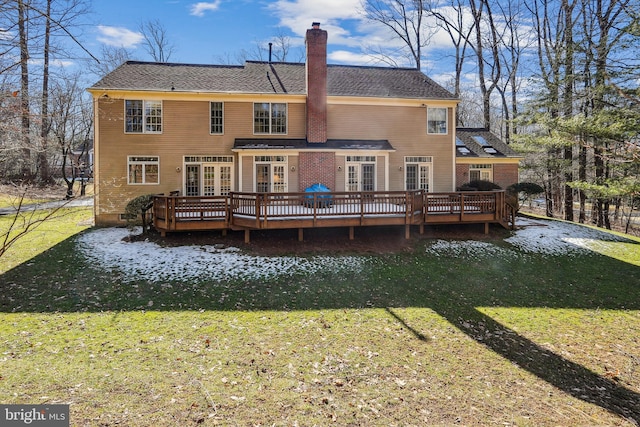 rear view of house featuring french doors, a chimney, a wooden deck, and a lawn