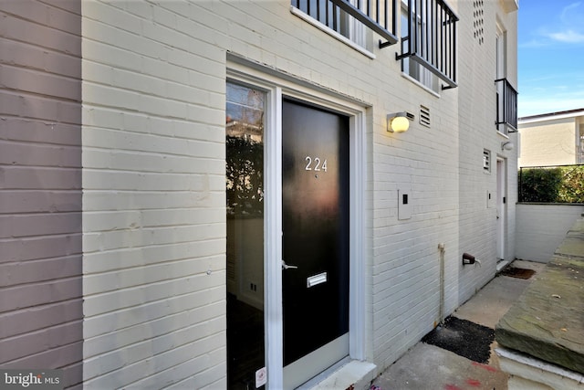 view of exterior entry featuring a balcony and brick siding