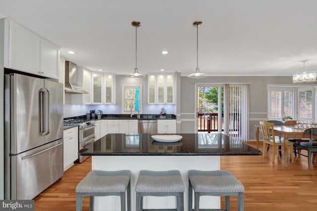 kitchen with wall chimney range hood, pendant lighting, stainless steel appliances, and a kitchen island