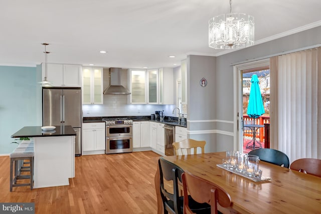 kitchen with appliances with stainless steel finishes, decorative light fixtures, a kitchen breakfast bar, and wall chimney range hood