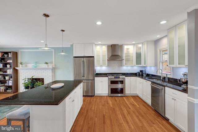 kitchen featuring decorative light fixtures, light hardwood / wood-style floors, stainless steel appliances, wall chimney exhaust hood, and white cabinets