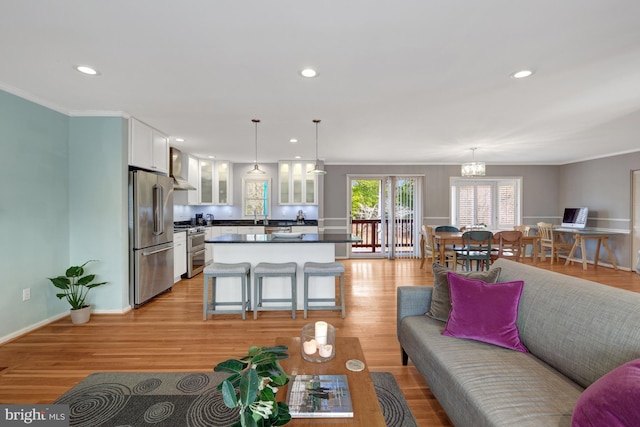 living room with a notable chandelier, light wood-type flooring, sink, and ornamental molding