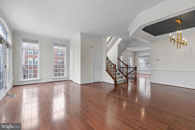 unfurnished living room featuring wood finished floors, baseboards, ornamental molding, stairway, and an inviting chandelier