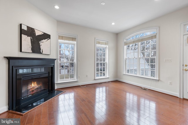 unfurnished living room featuring a glass covered fireplace, plenty of natural light, wood finished floors, and baseboards