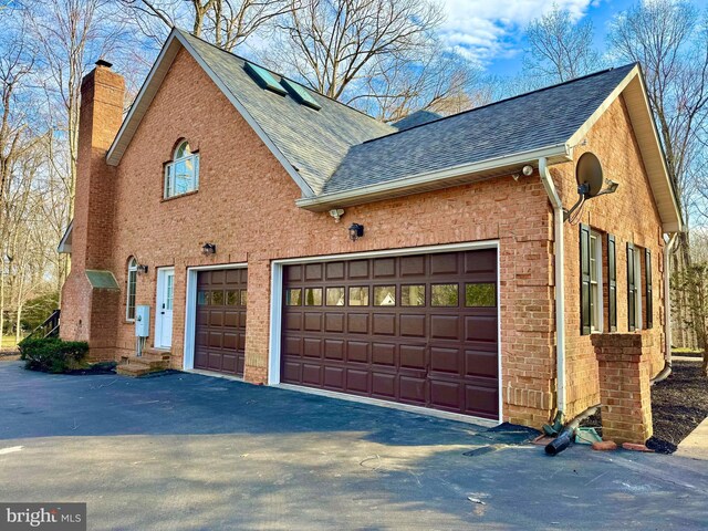 exterior space featuring a shingled roof, a chimney, aphalt driveway, and brick siding