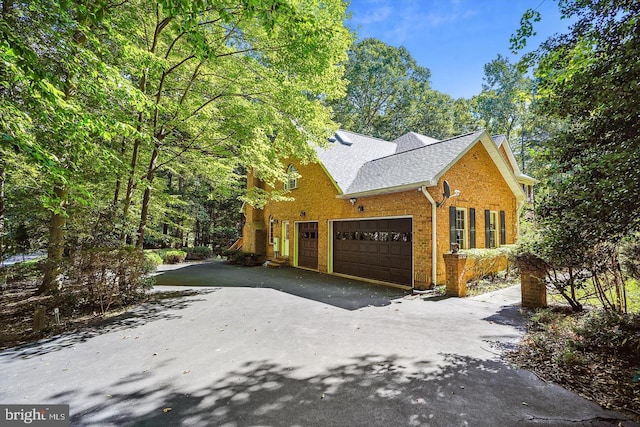 view of property exterior with a shingled roof, aphalt driveway, and brick siding