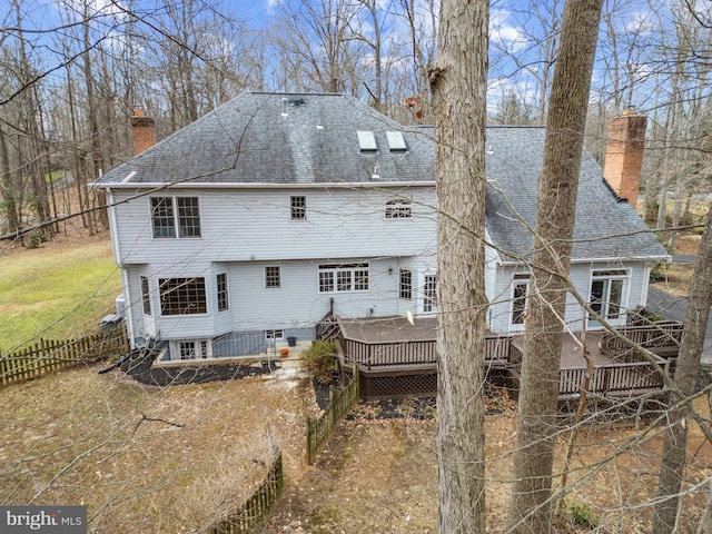 back of house with a shingled roof, a chimney, fence, and a deck