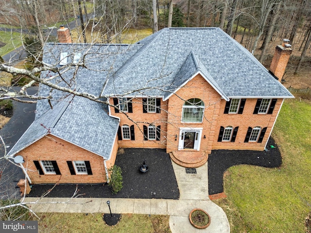 view of front of house with roof with shingles, brick siding, a chimney, and a front yard