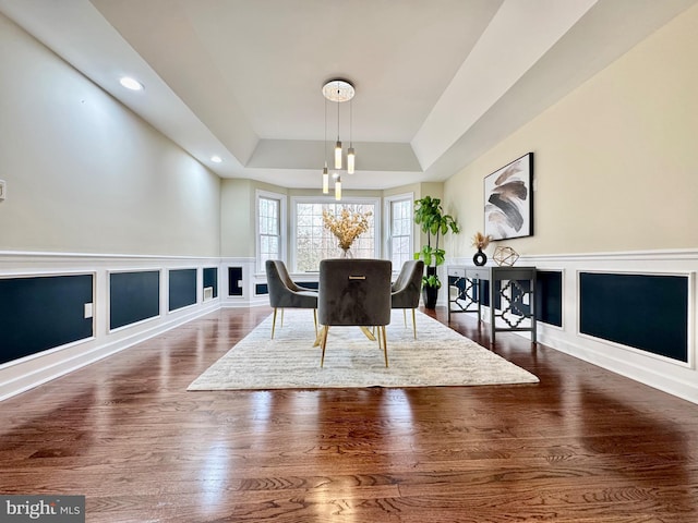 dining area with a decorative wall, dark wood-style flooring, a raised ceiling, and recessed lighting