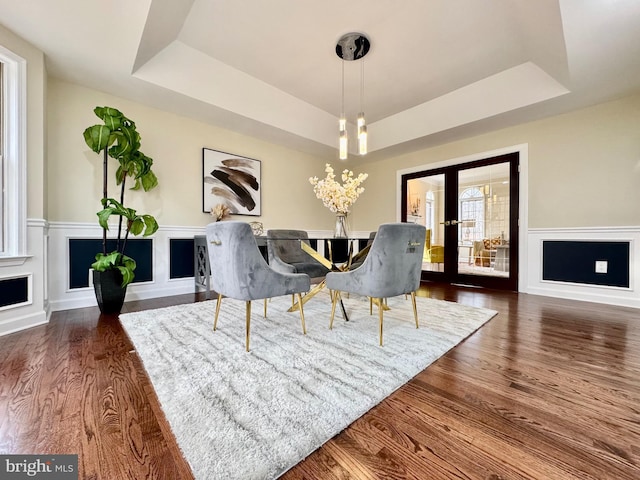 dining room with a wainscoted wall, a raised ceiling, dark wood finished floors, and a decorative wall