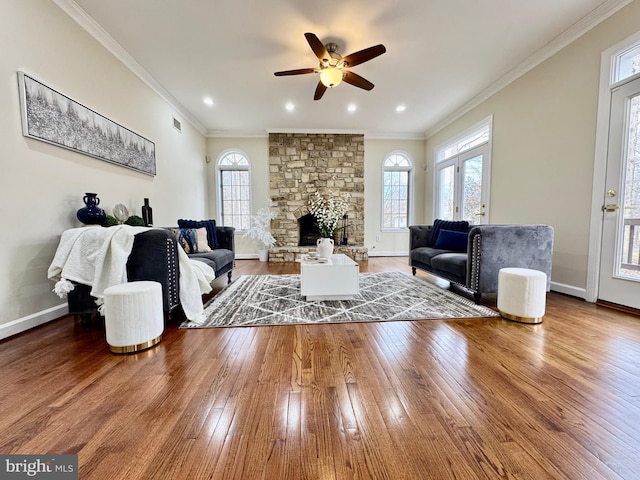 living area featuring baseboards, visible vents, ornamental molding, wood finished floors, and a stone fireplace