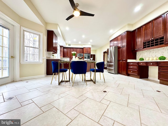 kitchen with reddish brown cabinets, decorative backsplash, a breakfast bar area, stainless steel appliances, and light countertops