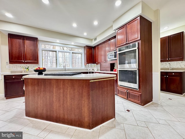 kitchen with a center island with sink, stainless steel appliances, light countertops, dark brown cabinets, and backsplash