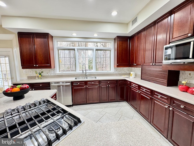 kitchen with reddish brown cabinets, light countertops, visible vents, appliances with stainless steel finishes, and a sink