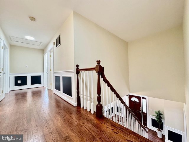 corridor featuring attic access, visible vents, wood finished floors, an upstairs landing, and a decorative wall