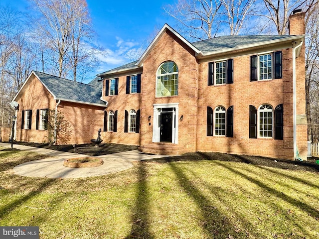 colonial inspired home with brick siding, a chimney, and a front lawn