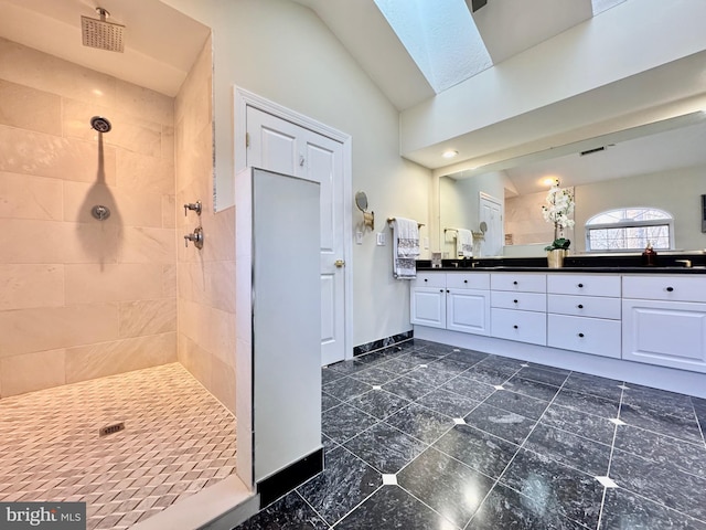 full bathroom featuring lofted ceiling with skylight, tiled shower, baseboards, and double vanity