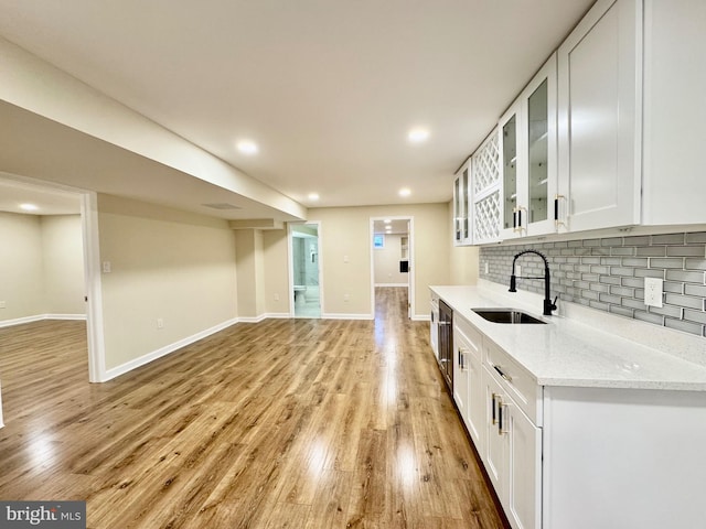 kitchen featuring light stone counters, tasteful backsplash, glass insert cabinets, white cabinetry, and a sink