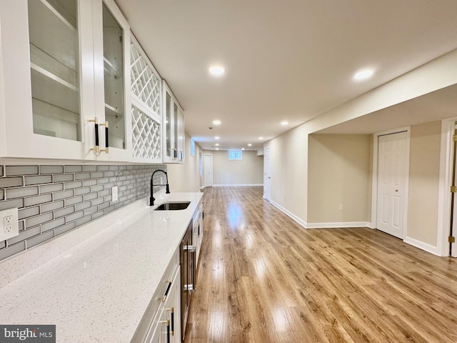 kitchen featuring a sink, white cabinets, light wood-type flooring, light stone countertops, and glass insert cabinets