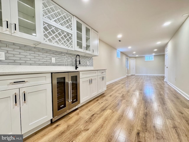 bar featuring beverage cooler, baseboards, decorative backsplash, light wood-style flooring, and wet bar