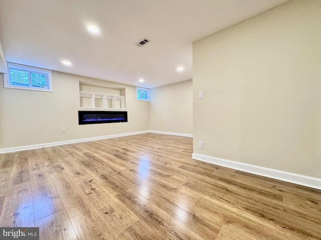 unfurnished living room with recessed lighting, wood finished floors, visible vents, baseboards, and a glass covered fireplace