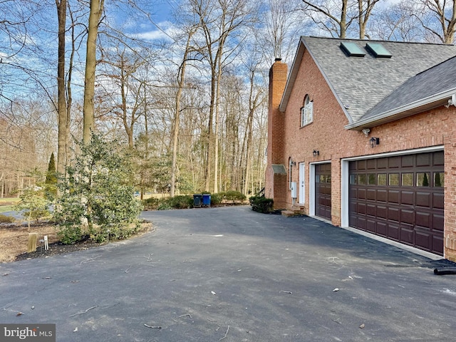 view of side of property with a shingled roof, brick siding, driveway, and a chimney