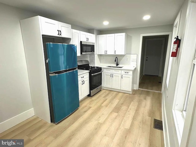 kitchen with appliances with stainless steel finishes, light hardwood / wood-style flooring, sink, and white cabinetry