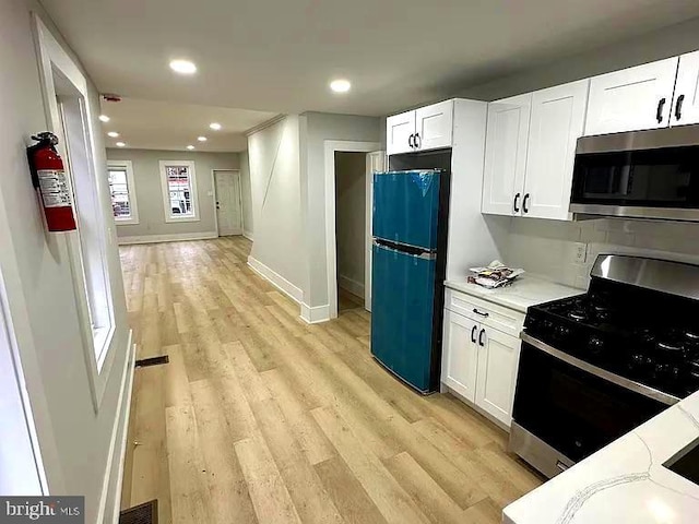 kitchen with appliances with stainless steel finishes, white cabinetry, and light hardwood / wood-style flooring