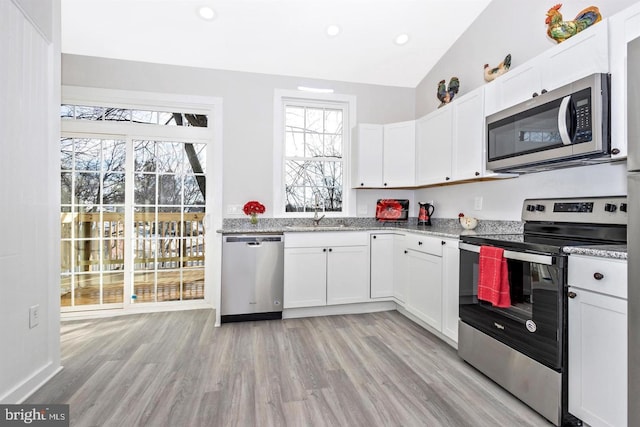 kitchen with appliances with stainless steel finishes, white cabinetry, light stone countertops, and sink