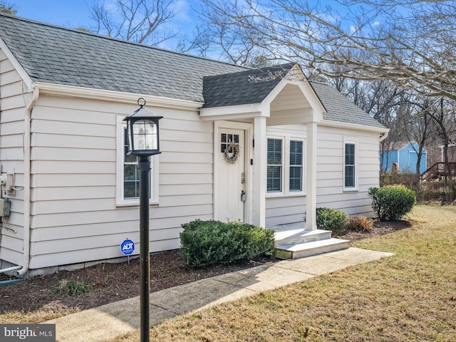 property entrance featuring a yard and roof with shingles