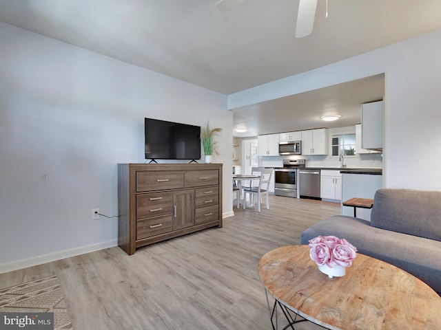 living room featuring light wood finished floors, ceiling fan, and baseboards