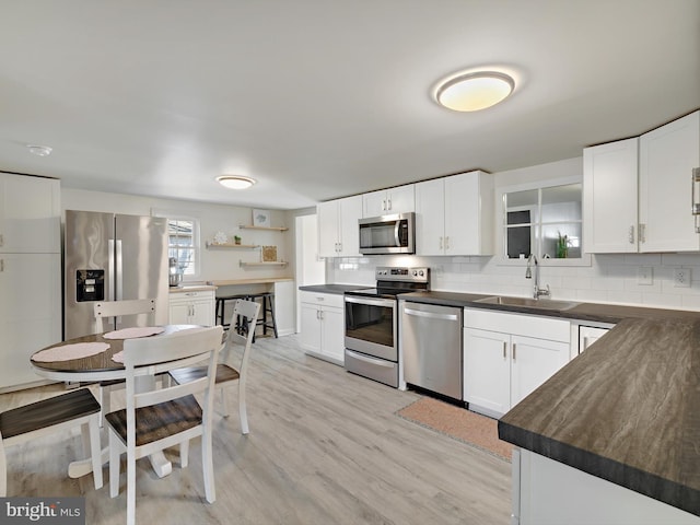 kitchen with light wood finished floors, dark countertops, decorative backsplash, appliances with stainless steel finishes, and a sink