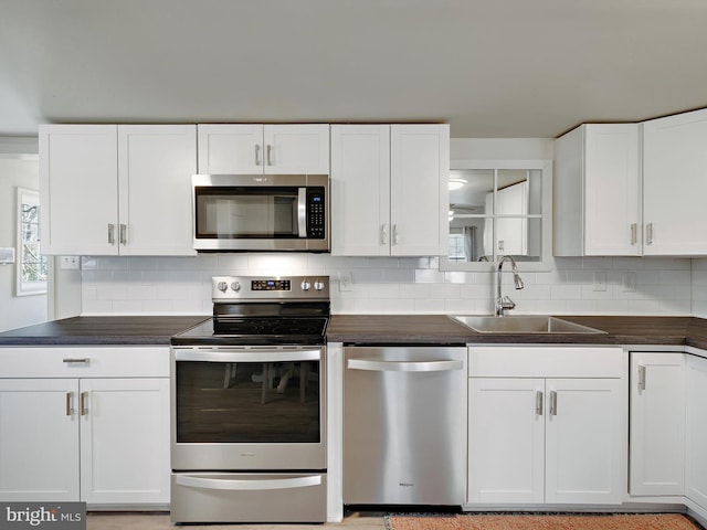 kitchen with dark countertops, backsplash, appliances with stainless steel finishes, white cabinetry, and a sink