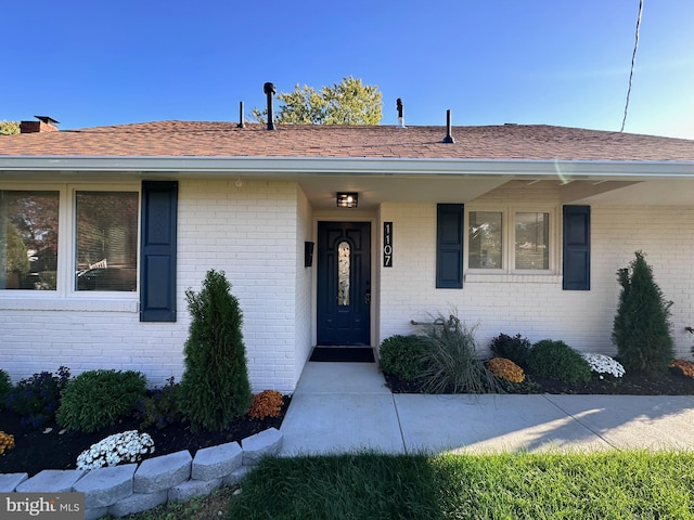 entrance to property featuring brick siding and roof with shingles