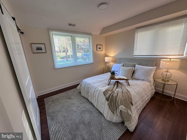 bedroom featuring wood finished floors, visible vents, baseboards, and a barn door