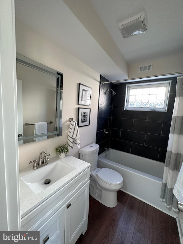 bathroom featuring toilet, wood finished floors, vanity, visible vents, and shower / bath combination with curtain