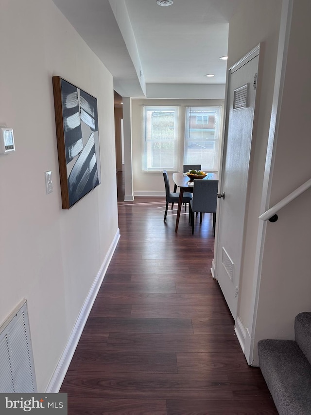 hallway with stairs, dark wood-type flooring, visible vents, and baseboards