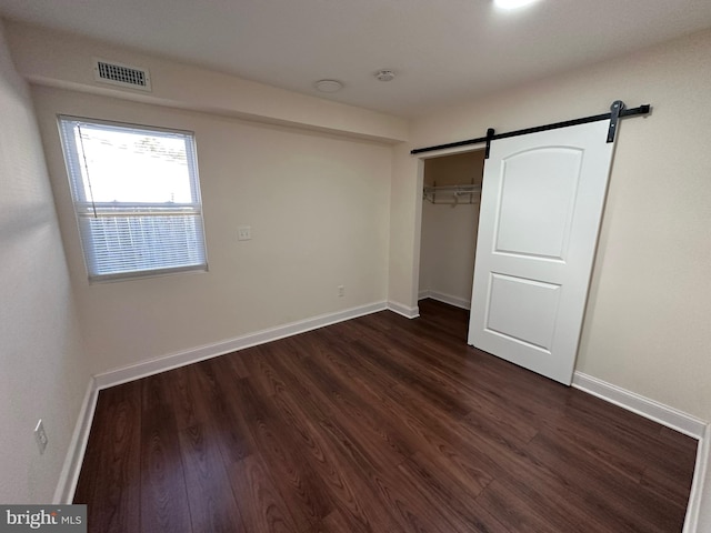 unfurnished bedroom with a barn door, visible vents, baseboards, a closet, and dark wood-style floors