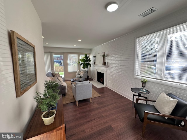 living room with visible vents, brick wall, a fireplace with flush hearth, dark wood-type flooring, and recessed lighting