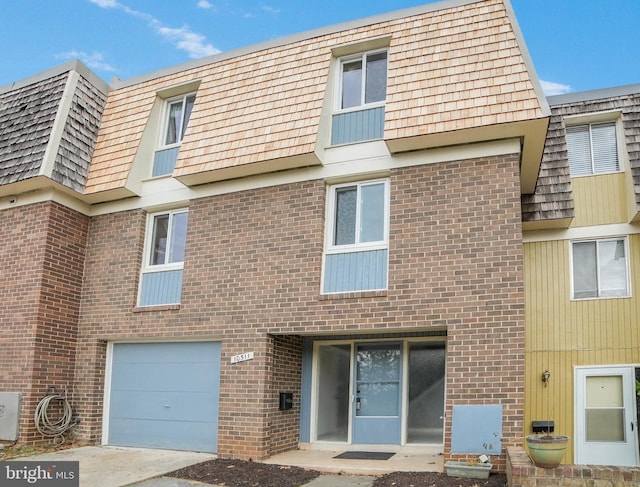 multi unit property with a garage, brick siding, and mansard roof