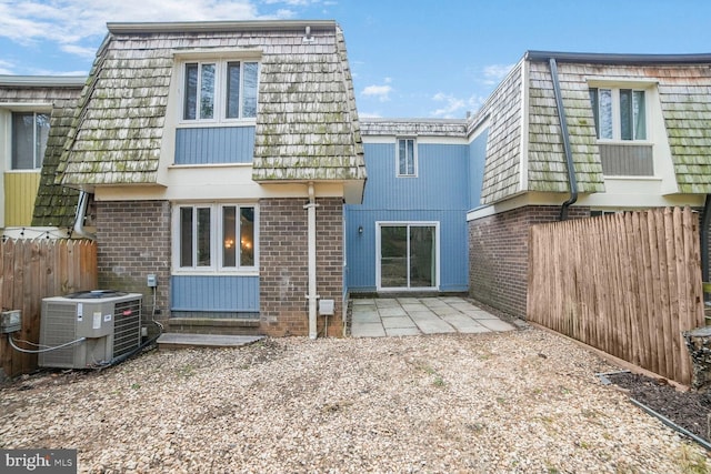 rear view of property with mansard roof, fence, cooling unit, a patio area, and brick siding