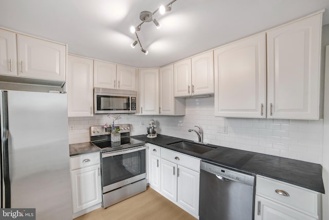 kitchen with stainless steel appliances, a sink, light wood-type flooring, decorative backsplash, and dark countertops