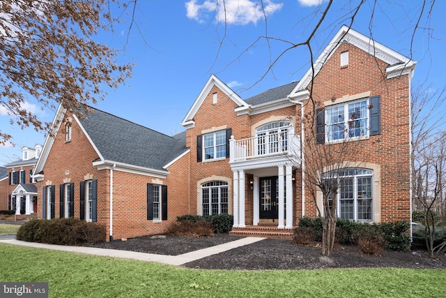 georgian-style home featuring brick siding, roof with shingles, and a front lawn