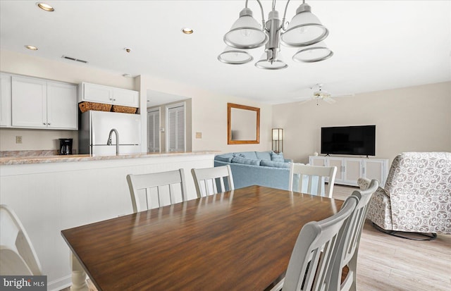 dining area featuring ceiling fan with notable chandelier and light hardwood / wood-style flooring