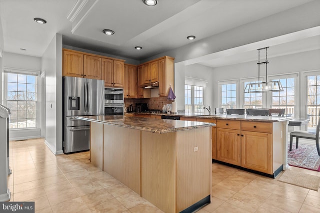 kitchen with a center island, dark stone countertops, appliances with stainless steel finishes, a peninsula, and a sink