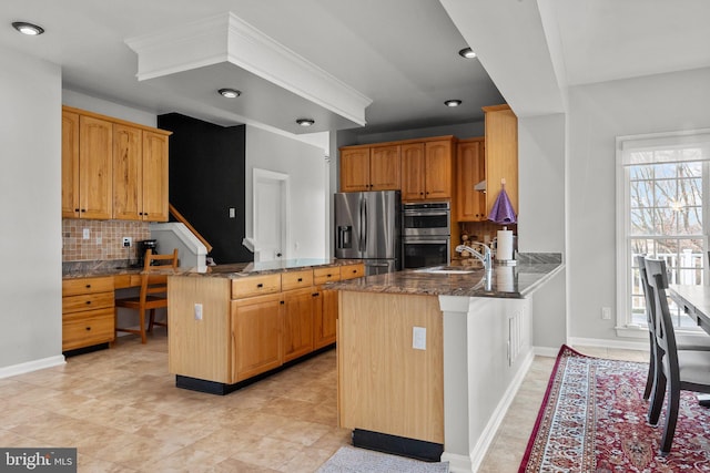 kitchen with a peninsula, dark stone counters, a sink, decorative backsplash, and stainless steel appliances