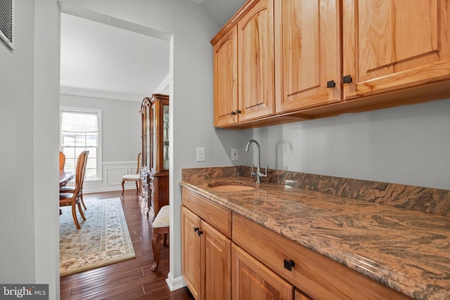 kitchen featuring dark wood finished floors, vaulted ceiling, dark stone countertops, wainscoting, and a sink